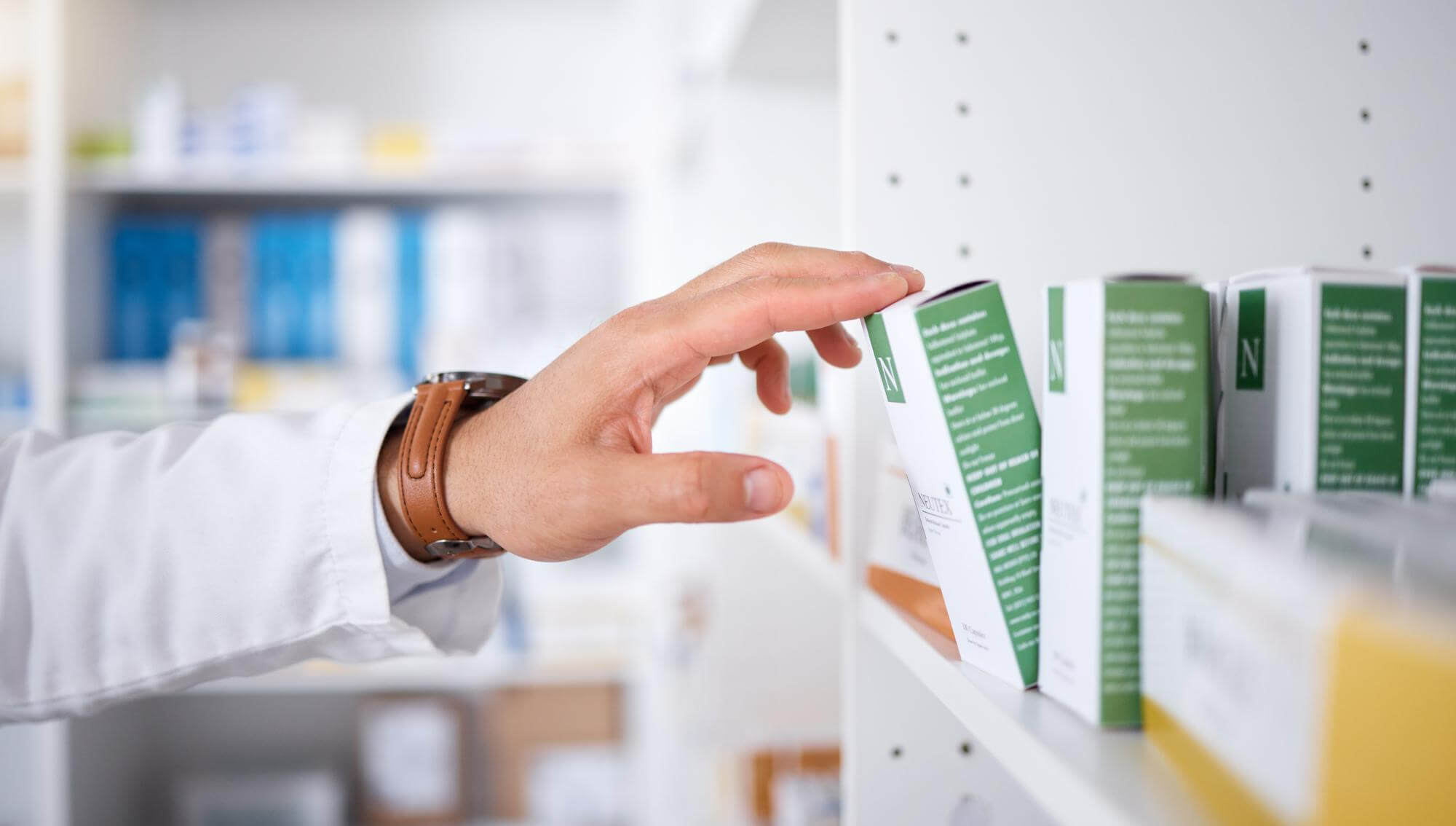Hand eines Apothekers greift nach einer Medikamentenschachtel im Regal einer Apotheke.