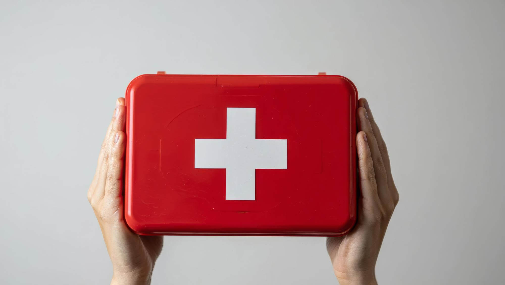 Eine Person hält eine rote Erste-Hilfe-Box mit einem weißen Kreuz auf der Vorderseite.